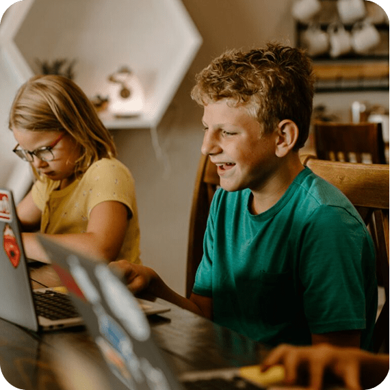 Two children sitting at a table using laptops